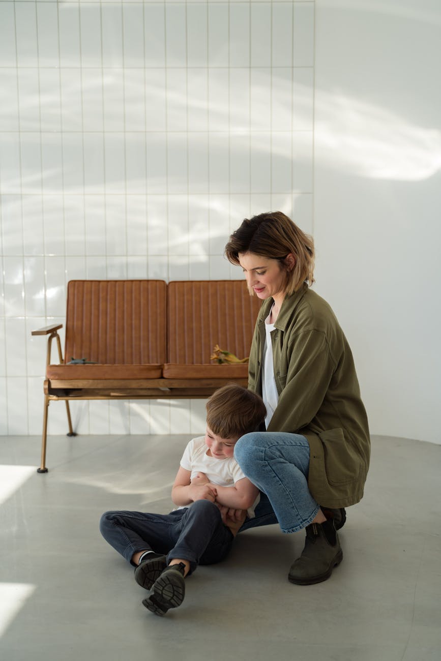 a mother crouching next to a boy sitting on the floor